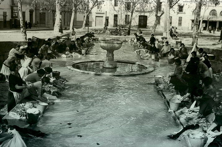 fotografia antiga del safareig - antic llavador de la Plaça de la Bassa de Xàtiva, amb persones llavant la roba a mà. Original de 1930, arxiu fotogràfic de la Impremta Papereria Marbau, acolorida digitalment per a la decoració de la bugaderia La Neta / LANETA
